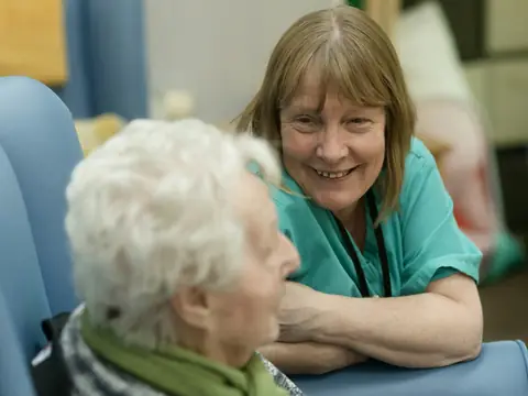 A care worker in scrubs chatting with an older woman