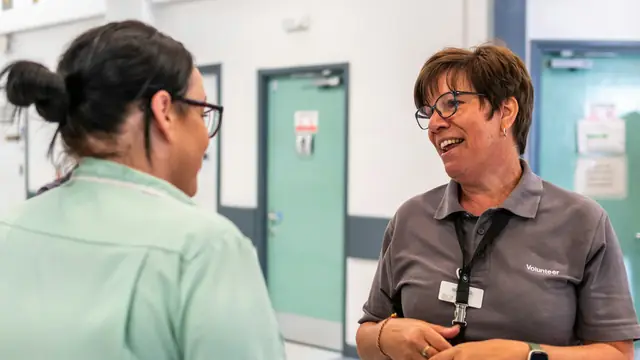 A hospital nurse chatting with a volunteer in a ward corridor