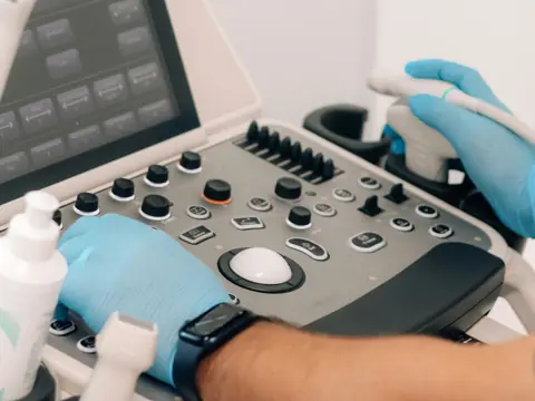 Gloved hands on the controls of an ultrasound machine